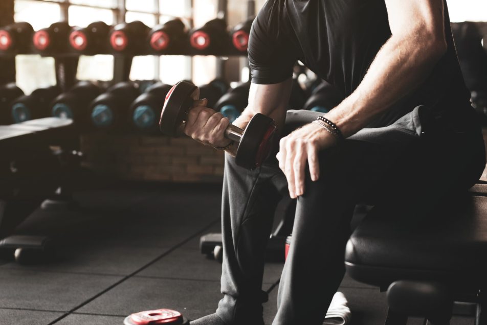 Handsome healthy man practicing with dumbbells in the gym. Man happy smiling while workout